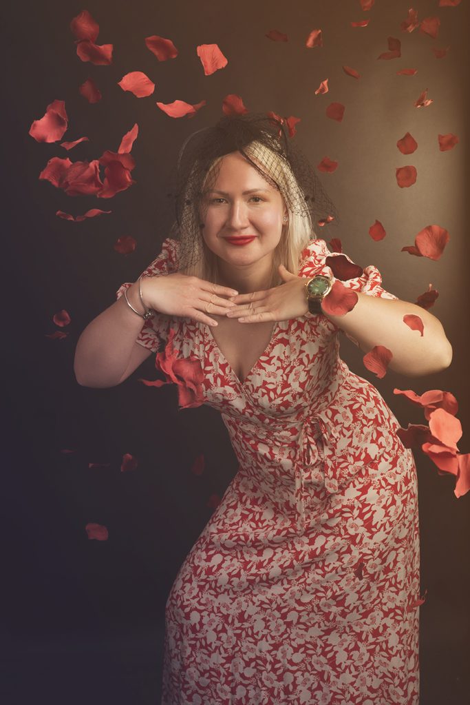 Frau in einem blumenmuster Kleid posiert vor fallenden Rosenblättern.