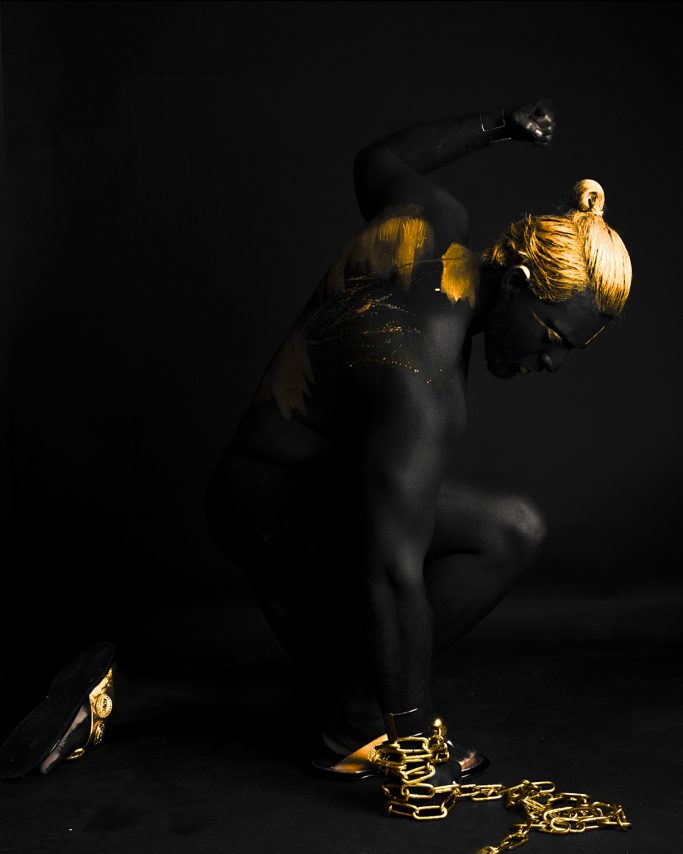 Eine künstlerisch dargestellte Figur mit goldener Körperfarbe und Ketten auf dunklem Hintergrund.