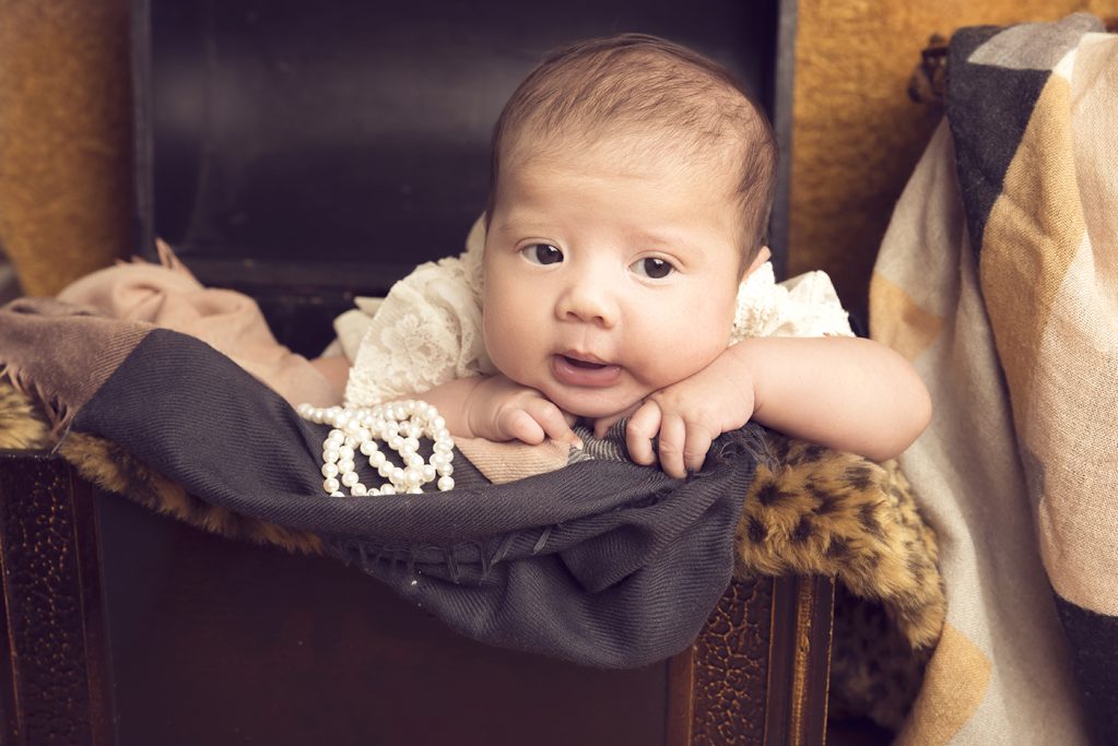 Ein lächelndes Baby liegt auf einer Decke in einem gepolsterten Korb.