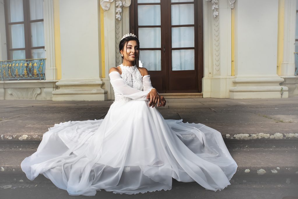 Eine Frau in einem weißen Kleid sitzt elegant vor einem historischen Gebäude.
