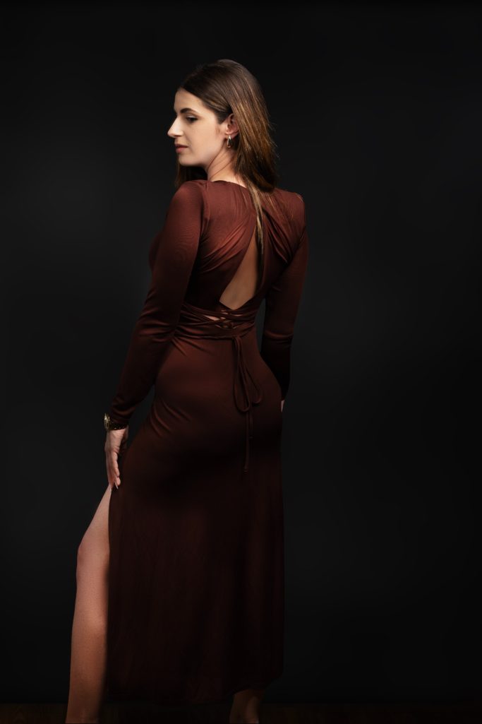 Frau in elegantem braunem Abendkleid mit offenem Rücken und seitlichem Schlitz.