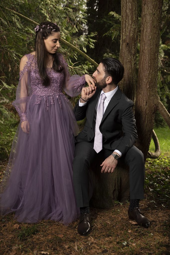Ein Mann in Anzug sitzt neben einer Frau in lila Abendkleid im Grünen.