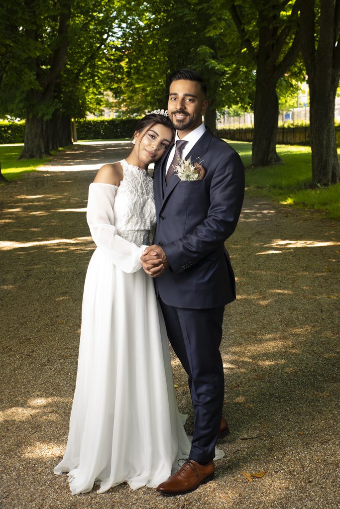 Hochzeitsfoto eines Paares in eleganter Kleidung, umgeben von Bäumen und Natur.