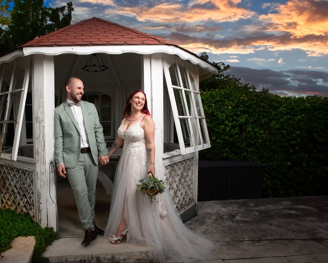 Ein frisch verheiratetes Paar posiert vor einem Pavillon bei Sonnenuntergang.
