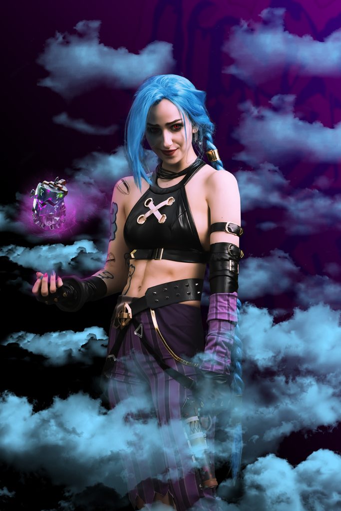 Farbige Person in Fantasy-Kostüm mit blauen Haaren und magischem Stab vor lila Hintergrund.
