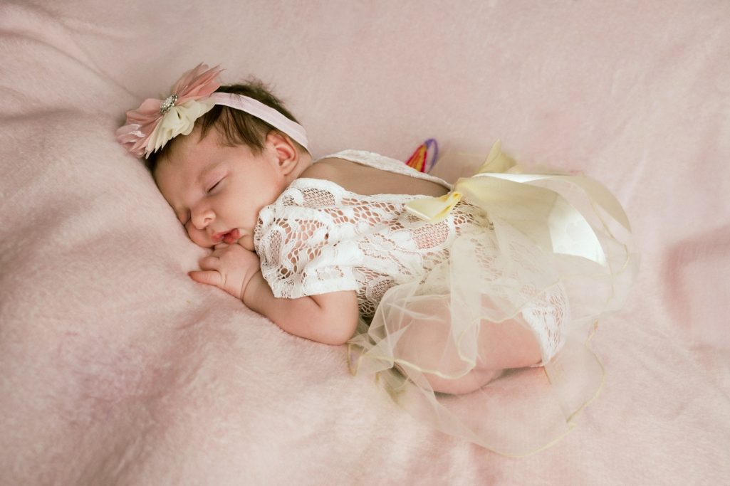 Neugeborenes Mädchen schläft in einem zarten Kleid mit einer Schleife auf einem rosa Hintergrund.